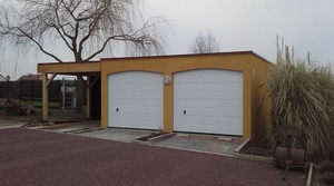 Garage double en béton avec un carport accolé. Couverture bacs acier. Deux portes sectionnelles, les linteaux du garage sont arrondis.