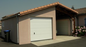 Garage en béton avec auvent accolé. Couverture tuiles, une porte sectionnelle et un châssis.