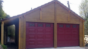 garage en béton aspect bois 2 pentes couverture tuiles entrée en pignon avec 2 portails sectionnelles et un auvent accolé en pignon