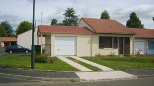 Garage en béton accolé à la maison avec un auvent accolé.